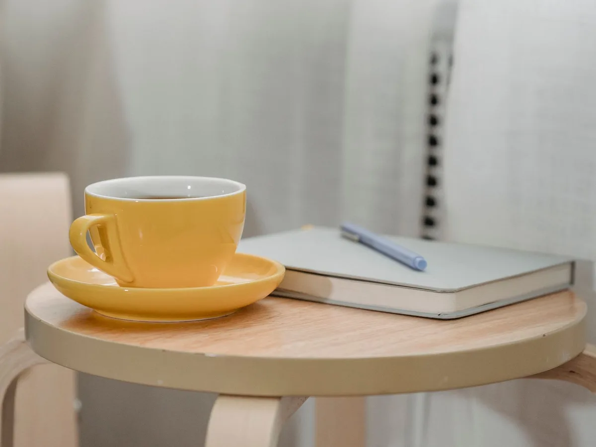 Yellow cup beside a notebook and pen on a small wooden table.